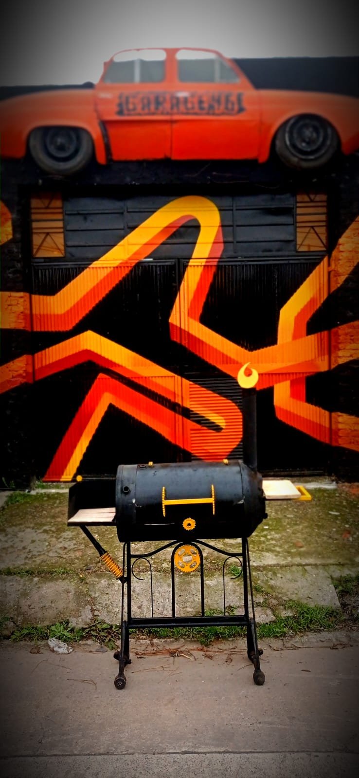Ahumador con chimenea frente al galpón pintado de naranja y negro